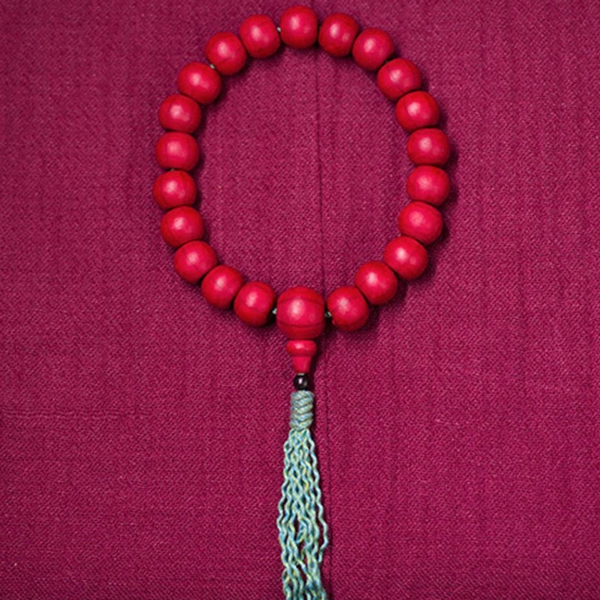 Prayer mala bead held between thumb and forefinger showing natural wood grain and finish