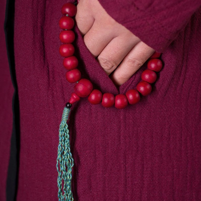 Wrist mala bracelet worn on hand against maroon robe showing spiritual meditation tool in use
