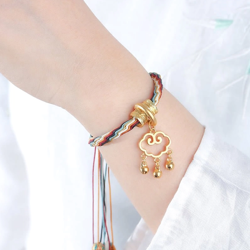 Adjustable braided Buddhist bracelet side view showing multicolor woven cord, antique gold hardware, hollow cloud lock pendant with hanging bells