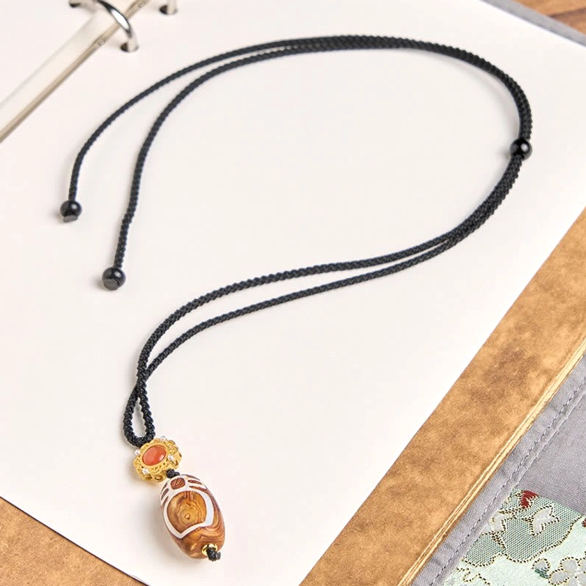 Adjustable Buddhist necklace showing complete nine-eye dzi bead pendant with black braided cord and sliding adjuster