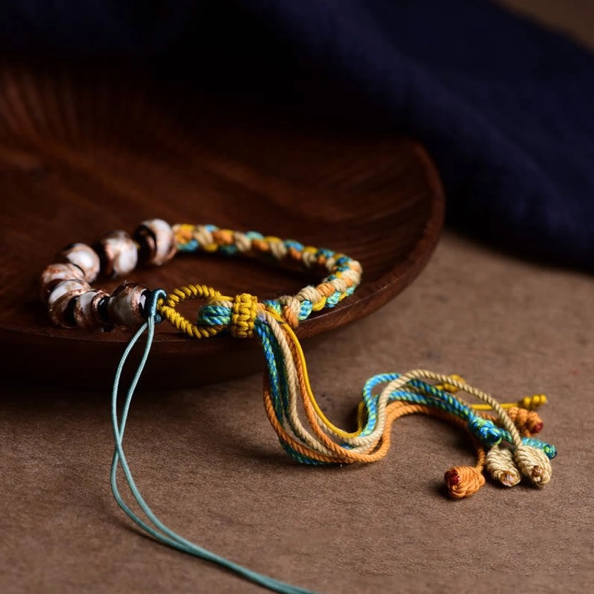 Side angle view of adjustable braided bracelet with loose cord tail on wooden surface