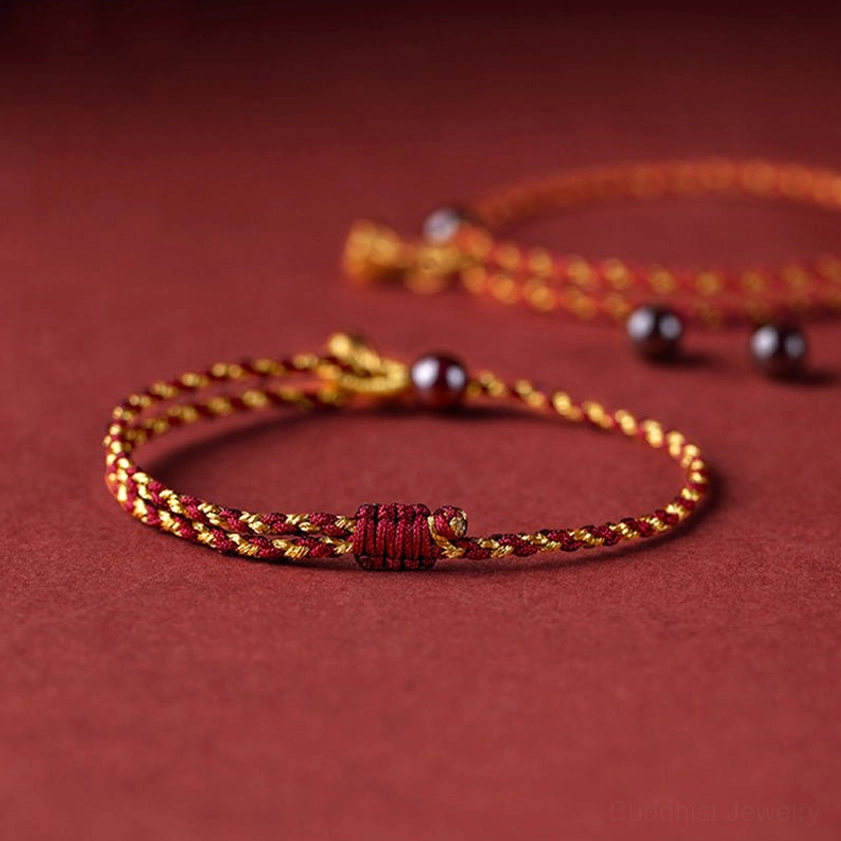 Adjustable red gold braided lotus bracelet showing red knot closure and decorative metal charms