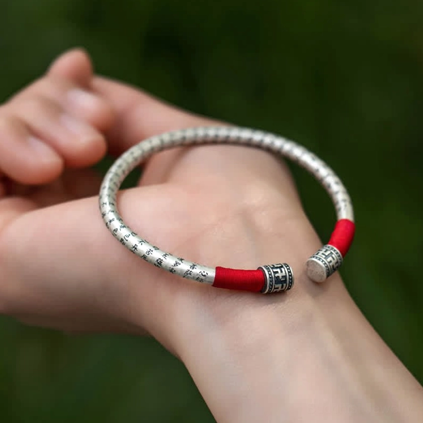 Open cuff Om Mani Padme Hum bracelet with dual red silk wraps, wrist display on green blurred background