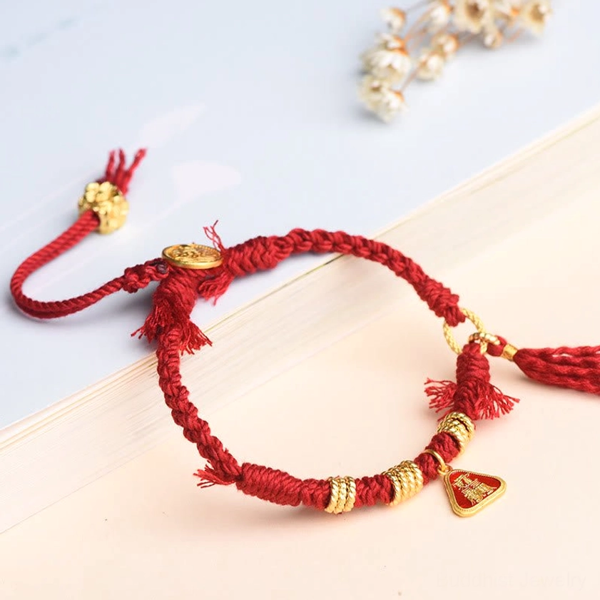 Adjustable red string bracelet with gold coil accents, triangle pendant charm, and tassel displayed on wooden table surface