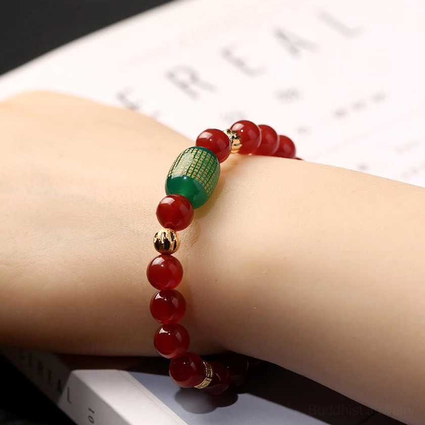 Red agate Buddhist bracelet worn on wrist with green sutra bead detail, lifestyle worn view against book background