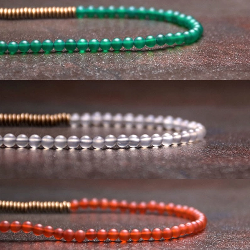 Single strand agate copper Buddhist bead bracelet flat lay top-down view on dark surface with multiple color stone options including red black green and white