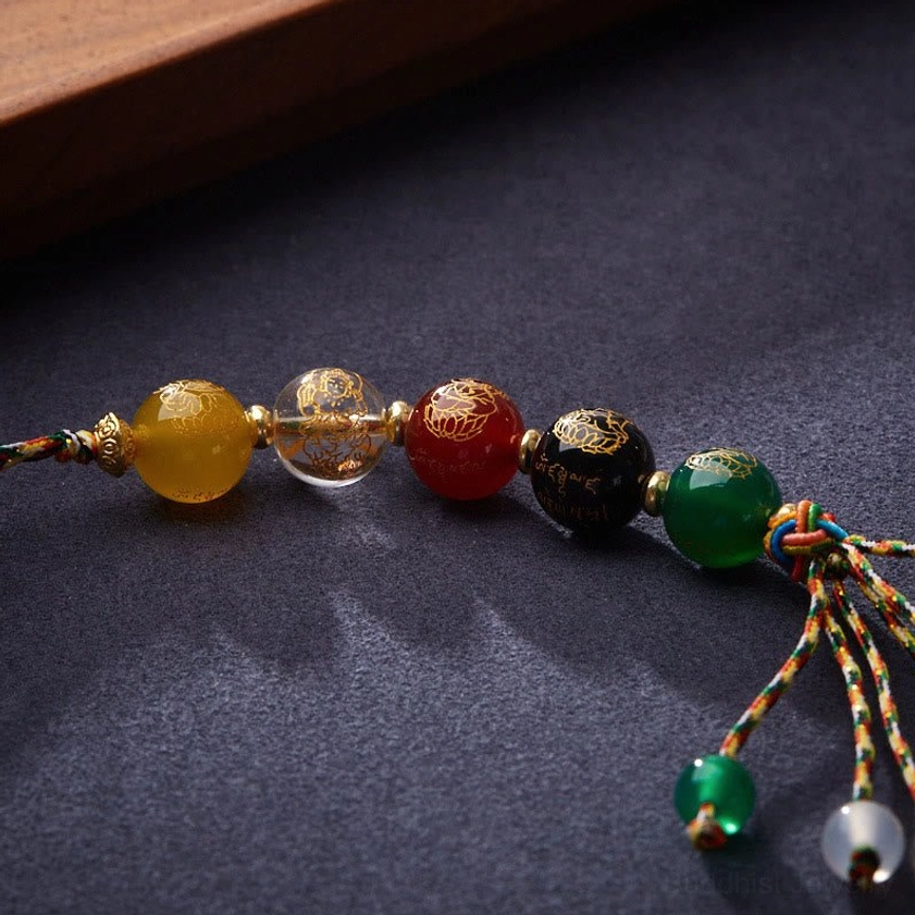 Close-up detail of Five Gods of Wealth agate beads with engraved patterns and colorful braided tassel on dark background