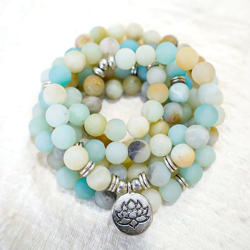 Amazonite lotus prayer mala flat lay overhead, featuring round matte stone beads in natural tones with silver spacers and engraved lotus metal charm