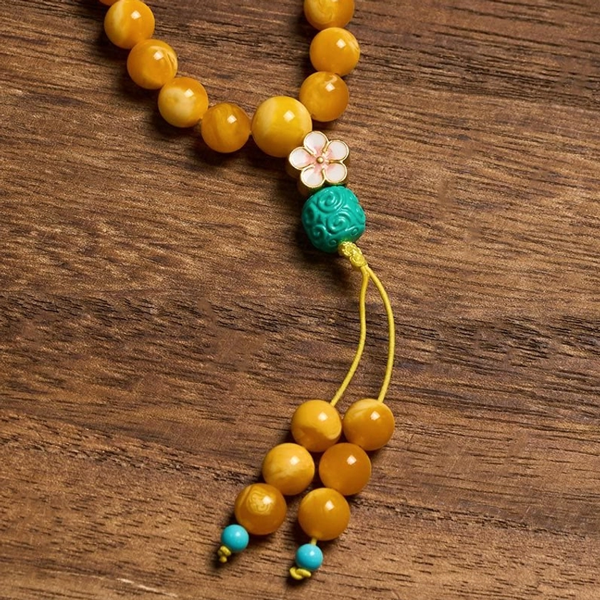 108-bead amber mala with carved turquoise guru bead and flower ornament detail on wooden table, flat lay lifestyle shot
