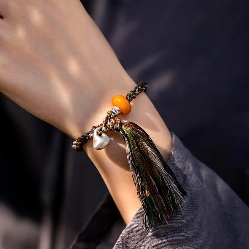 Buddhist protection bracelet worn on wrist showing tassel pendant and silver charm close-up