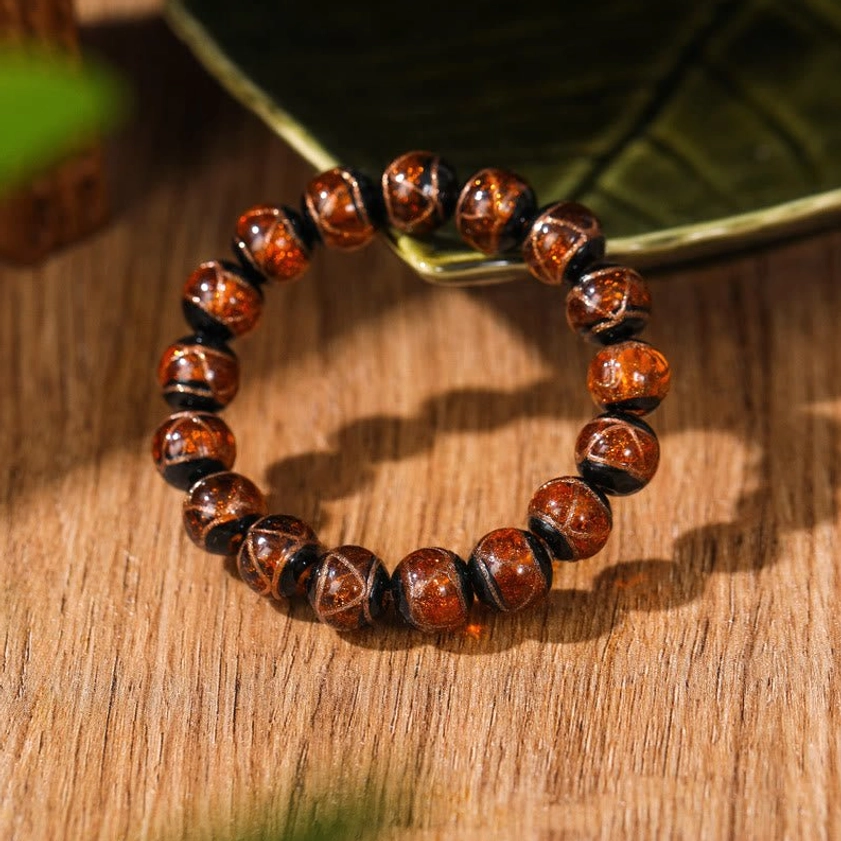 Smooth amber-brown glossy liuli glass Buddhist bracelet with natural finish on wooden table flat lay