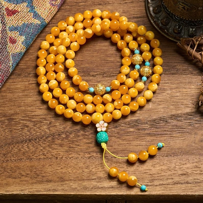 108-bead amber Buddhist prayer mala with turquoise accents and guru bead, displayed on wooden surface with ethnic fabric