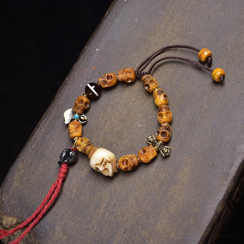 Amber tone carved barrel skull bead bracelet with red tassel and white resin skull
