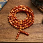 108 amber Buddhist prayer mala beads flat lay with tassel pendant on wooden surface
