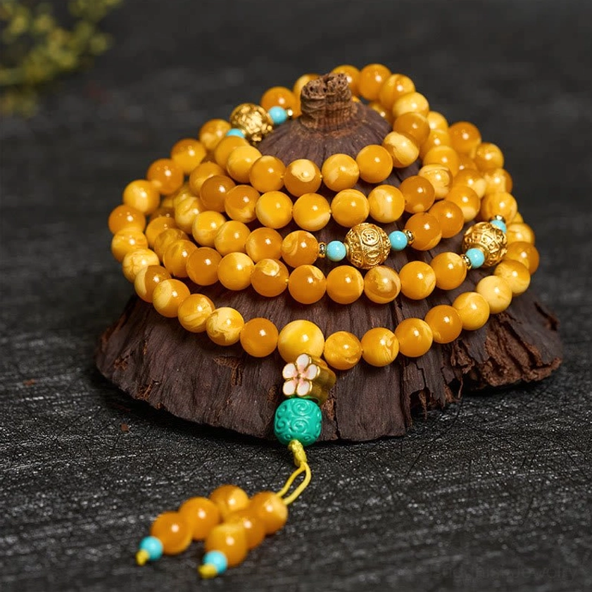 Close-up overhead view of amber prayer mala showing detailed bead texture, gold metal spacers, turquoise decorative beads, and hanging tassel