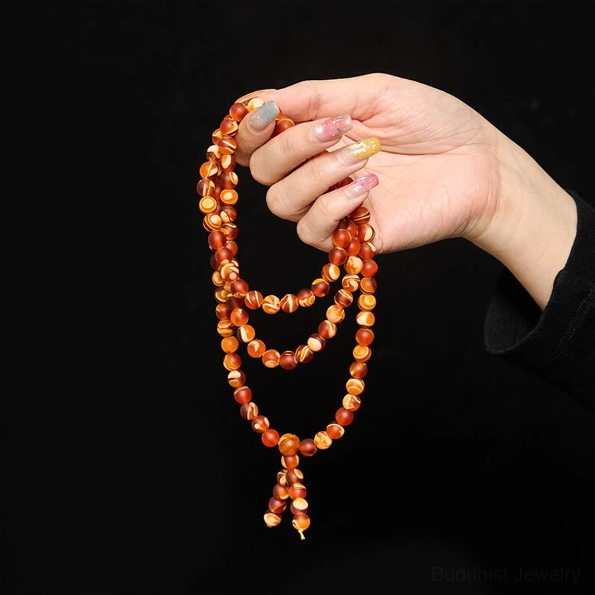 Coiled amber mala beads held in female hand showing two-tone round beads and strands