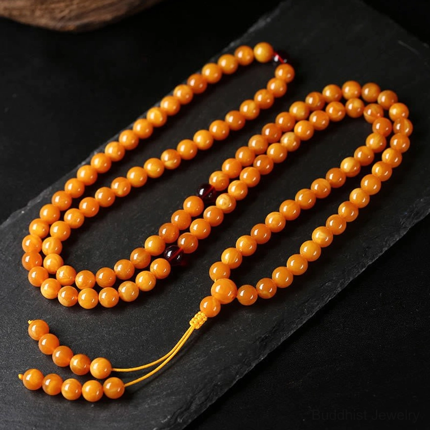 Two amber Buddhist mala bracelets with red spacer beads and golden tassels on dark background