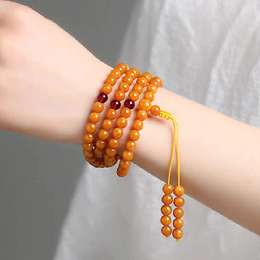 Worn amber Buddhist mala bracelet wrapped around wrist showing 108 beads with yellow tassel pendant