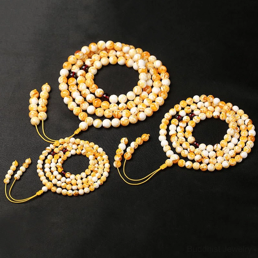 Four small amber mala bracelets flat lay black background yellow and off-white round beads