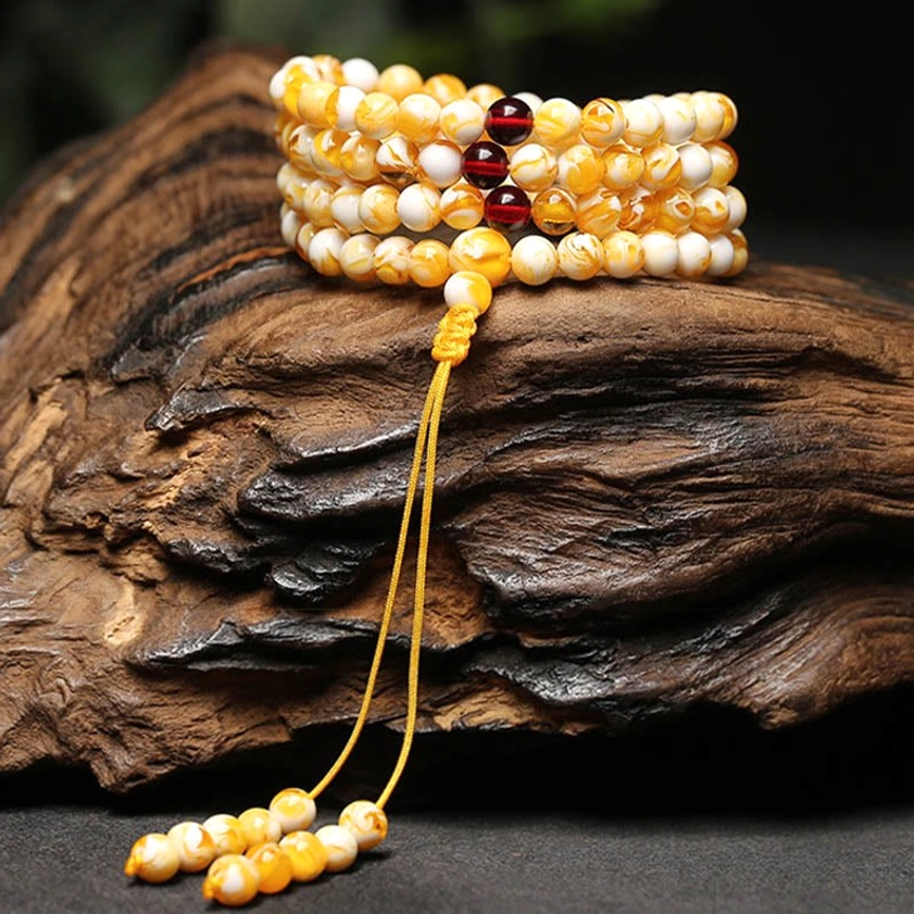 Multiple amber mala bracelets and long necklace layered display wooden slab white and amber beads