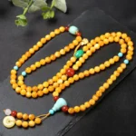 108 bead amber Buddhist mala necklace with turquoise guru bead and red agate accents, flat lay overhead view