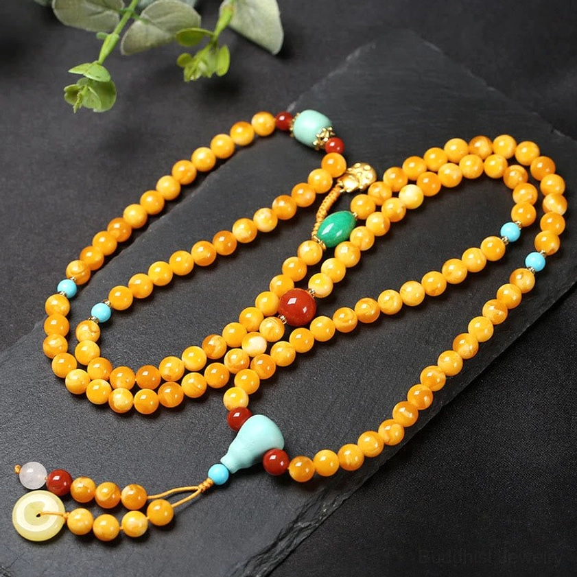 108 bead amber Buddhist mala necklace with turquoise guru bead and red agate accents, flat lay overhead view
