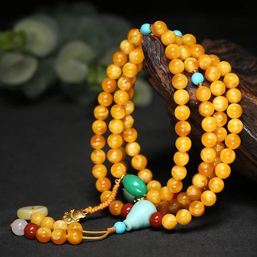 Coiled amber mala necklace displayed at angle with tasseled pendant and mixed gemstone accents on natural wood surface