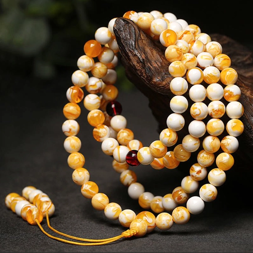 Buddhist amber mala necklace oblique side view dark wood background with mixed white and brown beads