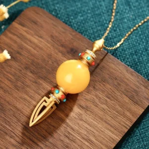 Gold plated amber dorje vajra pendant necklace, top-down view on wooden coaster with spiritual backdrop