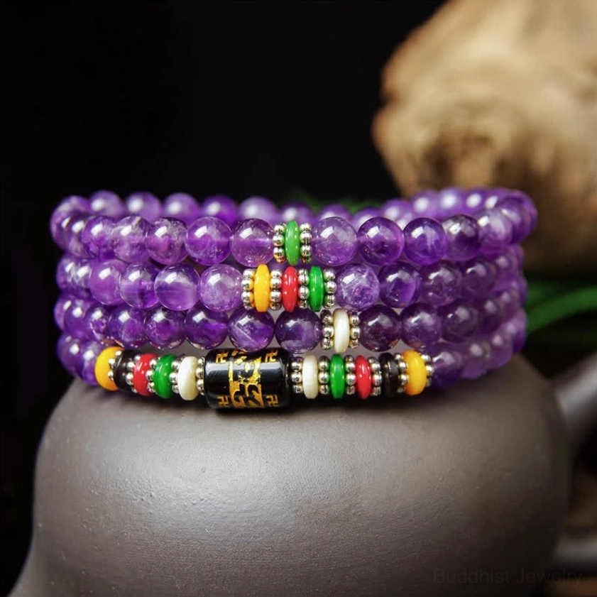 Handcrafted amethyst 108 bead mala bracelet with black metal mantra beads and colorful spacers arranged beside purple clay teapot