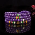 Amethyst 108 bead mala bracelet with colorful spacers and Om Mani Padme Hum mantra beads, top-down view on dark mirrored background