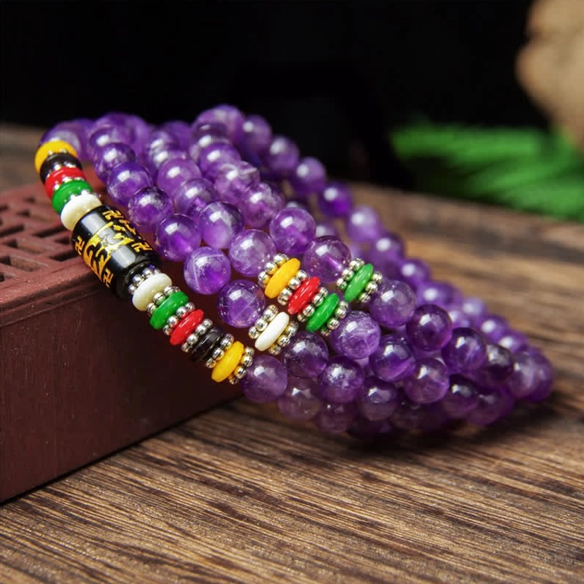 Round amethyst prayer beads mala bracelet with metal mantra decorative beads and colorful spacers on mirrored dark surface