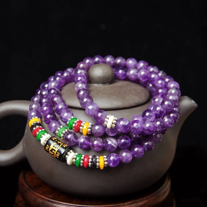 Round smooth amethyst prayer mala beads with decorative mantra spacer beads, top-down flat view on dark background with clay pot