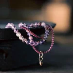 Multi-layer amethyst and garnet beaded bracelet with gold charm, displayed on dark tray showing 6mm purple amethyst beads and 4mm red garnet beads