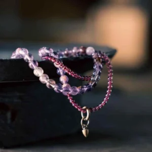 Multi-layer amethyst and garnet beaded bracelet with gold charm, displayed on dark tray showing 6mm purple amethyst beads and 4mm red garnet beads