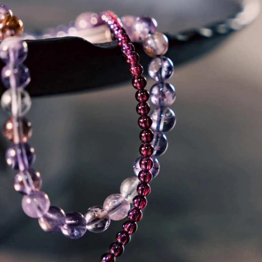 Extreme close-up detail of faceted amethyst and small red garnet beads with metal accent bar showing craftsmanship and natural stone texture