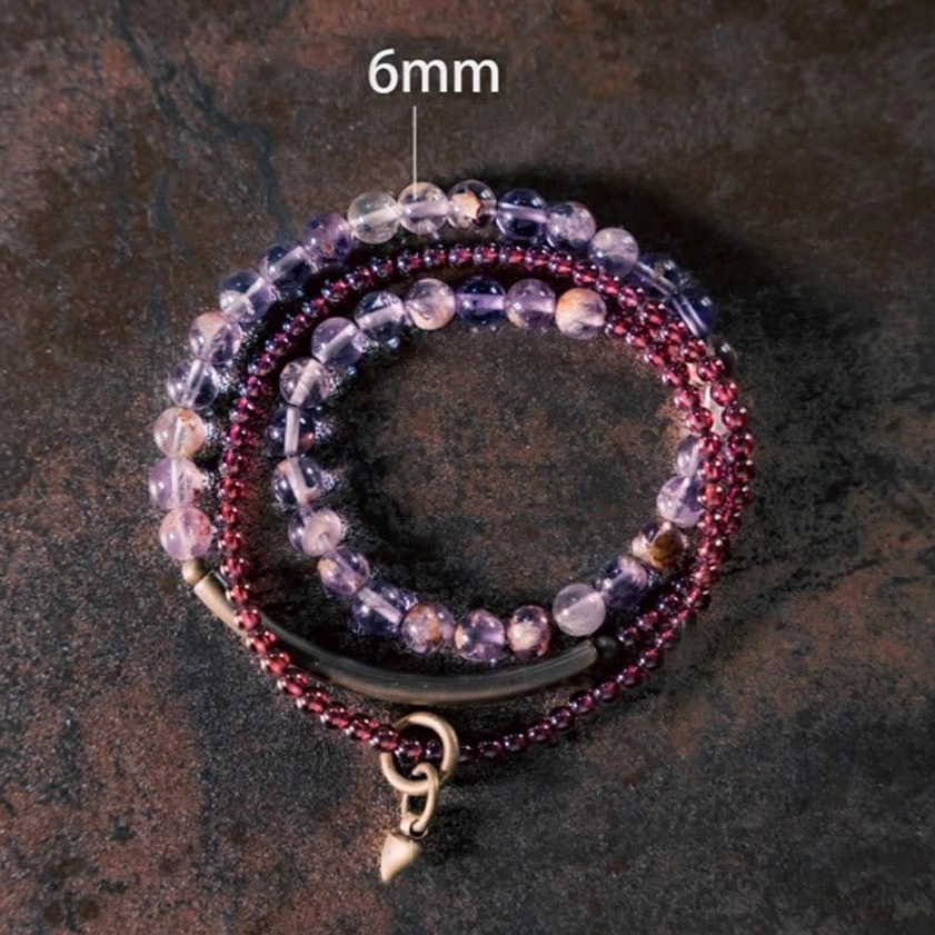 Top-down close-up of amethyst and garnet layered beaded bracelet showing 6mm labeled amethyst beads, 4mm garnet beads, and drop charm on dark surface