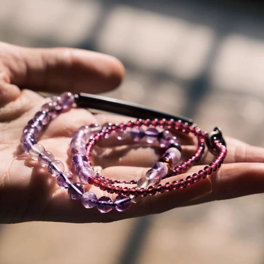 Amethyst and garnet layered beaded bracelets held in human hand with natural lighting, displaying gold charm accent and bead arrangement