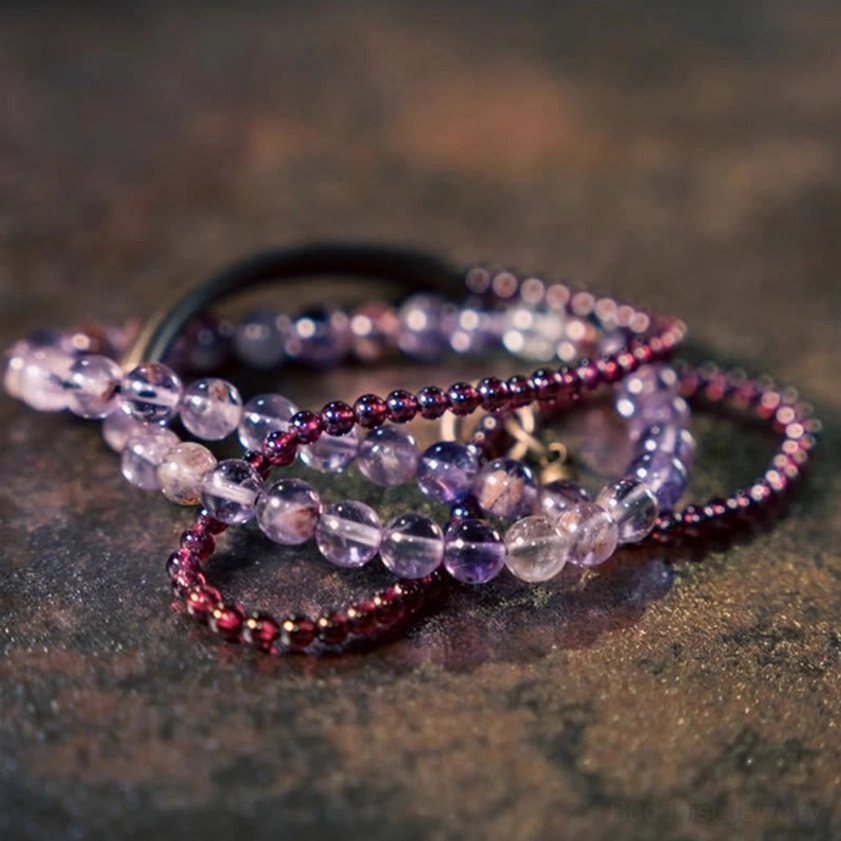 Multi-strand amethyst and garnet gemstone bracelets close-up on dark textured surface with faceted purple and red beads and metal bar accent