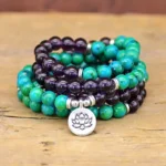 Amethyst and green aventurine lotus bracelet with silver pendant displayed on wooden surface, showing dual-strand spiritual design