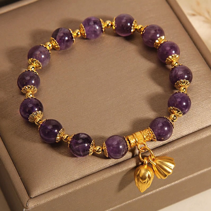 Natural amethyst lotus bracelet overhead view with matte gold accents and deep purple stones on stacked boxes