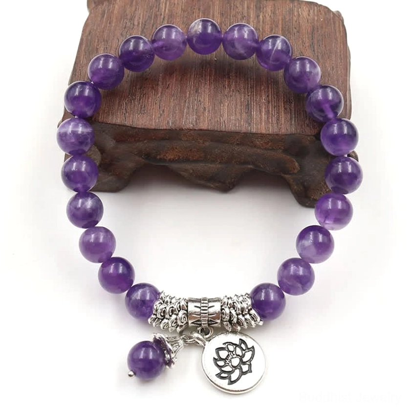Amethyst beaded bracelet top-down view on wooden display showing full circular strand with silver decorative clasp and lotus charm