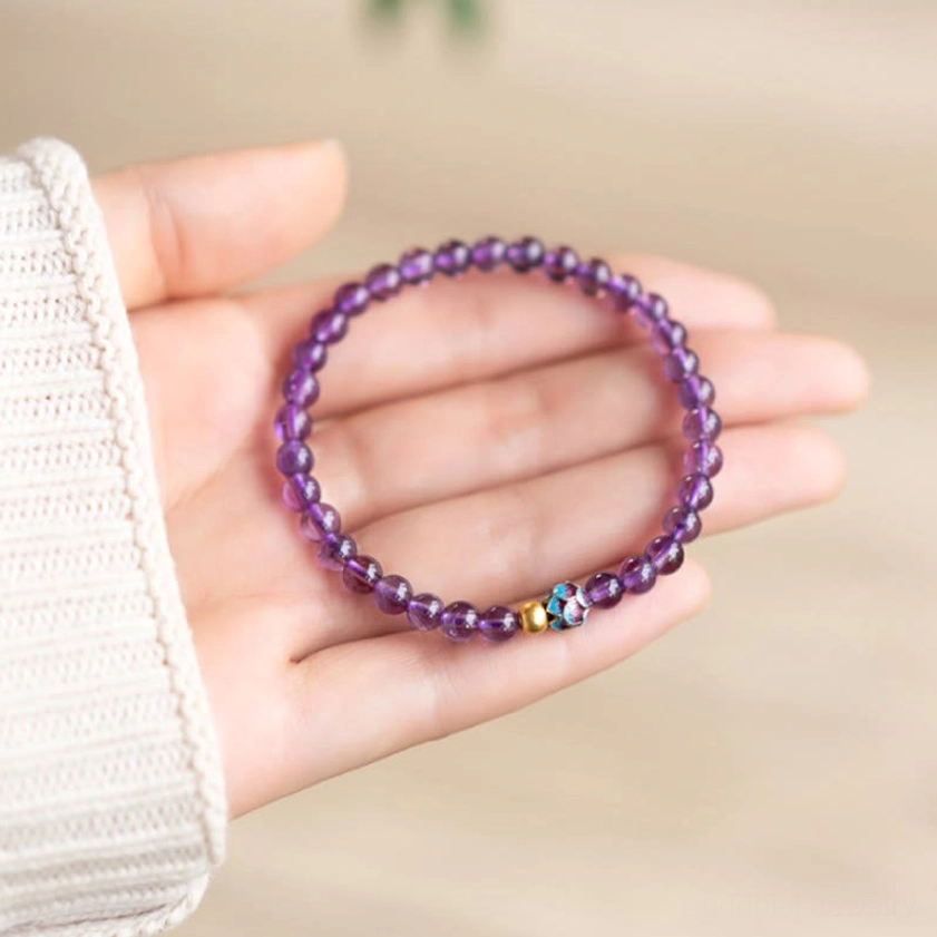 Amethyst beaded bracelet in palm showing smooth round purple crystal beads and enamel gold spacer details