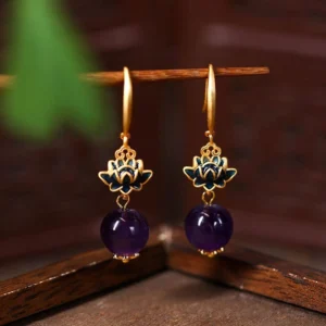 Amethyst lotus drop earrings hanging view with gold hooks and blue enamel lotus charm on wooden display stand