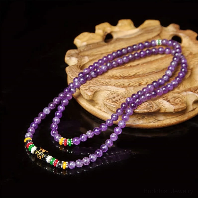 Handcrafted amethyst mala bracelet with metal mantra beads displayed on wooden table with green plant background and natural lighting