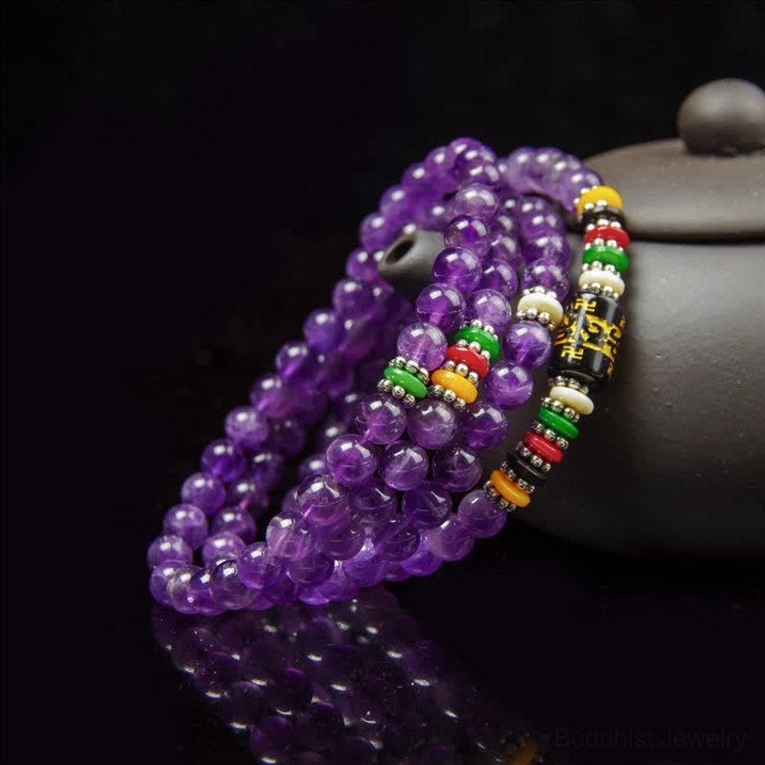 Deep purple amethyst 108 bead prayer mala with mantra spacer beads and mirror reflection on dark background with clay teapot