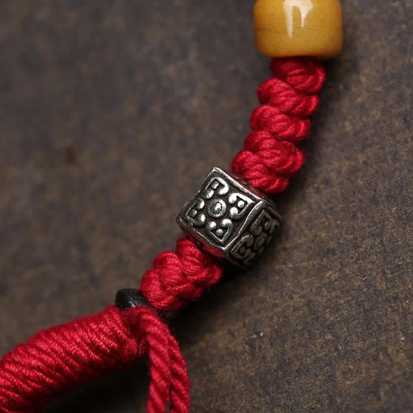 Close-up detail of red braided cord, carved metal Buddha pendant bead, and yellow agate stone accents on the Buddhist protection bracelet
