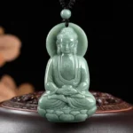 Amitabha Buddha jade pendant front view displayed on carved wooden base, showing green jade with lotus pedestal and chest swastika carving