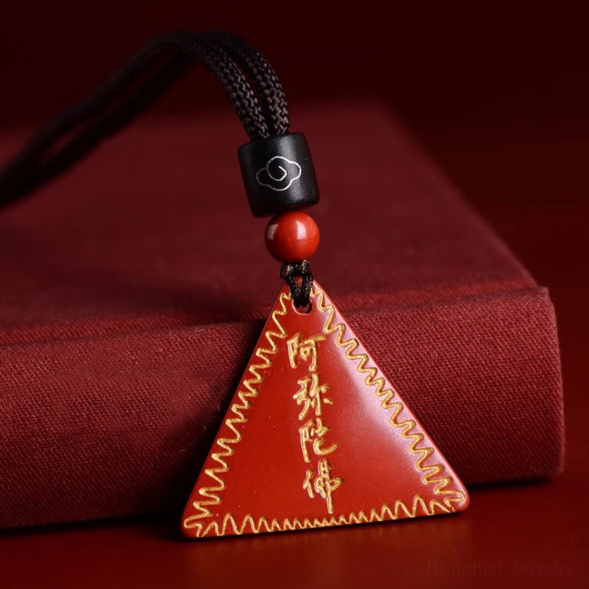 Cinnabar Amitabha Buddhist charm pendant resting on red fabric display box with black braided cord