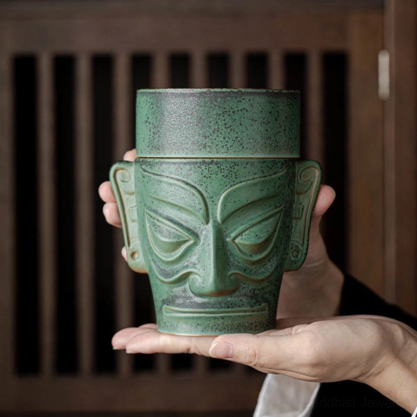 Handcrafted ceramic incense burner held in hands, showing stylized mask relief design with matte speckled green finish and fitted lid